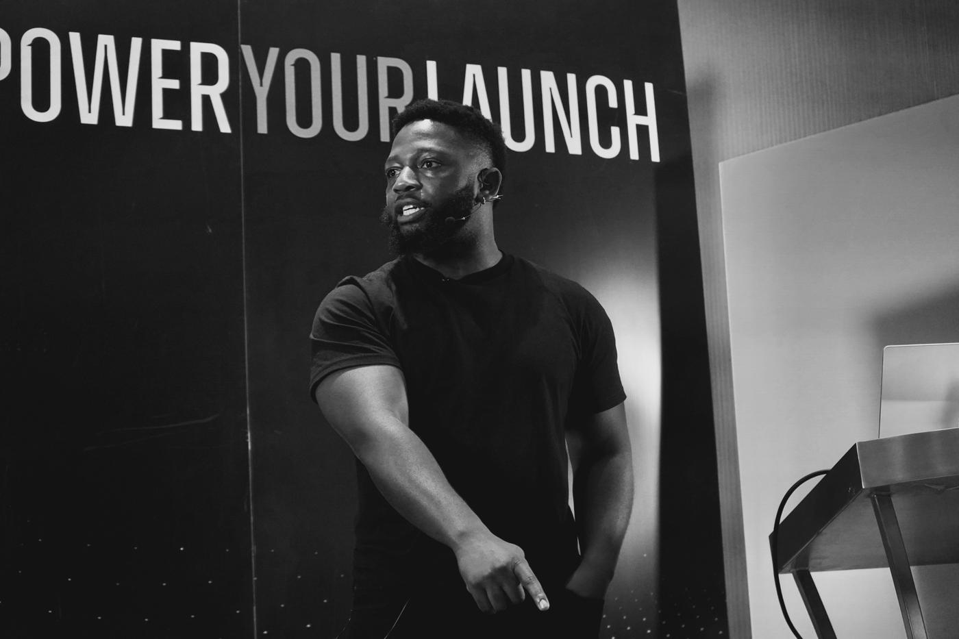 Abu Fofanah speaking on stage in front of a Power Your Launch sign